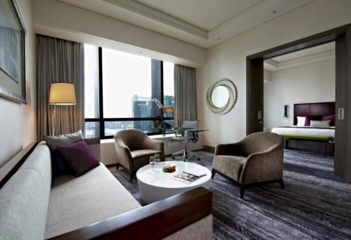 Carlton City Hotel Singapore suite. Gay-friendly hotel room with seating area, desk, and view into the bedroom. Modern design.