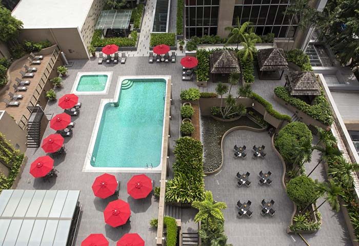 Carlton Hotel Singapore pool area, a gay-friendly hotel. Aerial view of the pool, red umbrellas, lounge chairs, and tropical landscaping.