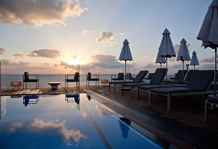 Carlton Tel Aviv Hotel luxury pool at sunset. Gay-friendly hotel on the beach with lounge chairs and ocean view. Perfect for gay travel.