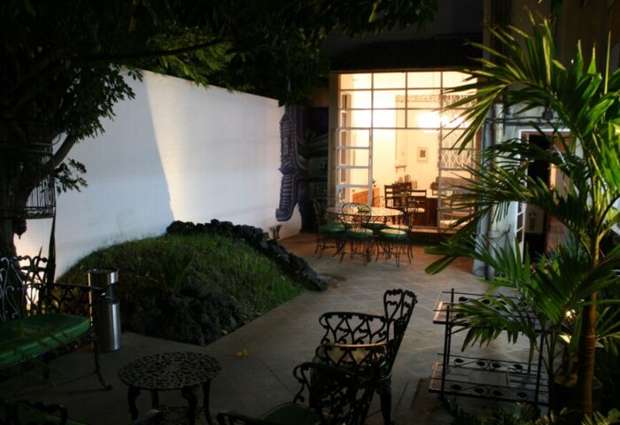Casa Comtesse's outdoor patio at night. This gay-friendly hotel features garden seating, a mural, and a view into the dining area.