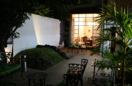 Casa Comtesse's outdoor patio at night. This gay-friendly hotel features garden seating, a mural, and a view into the dining area.