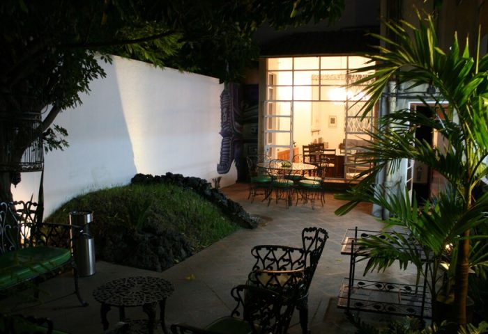 Casa Comtesse's outdoor patio at night. This gay-friendly hotel features garden seating, a mural, and a view into the dining area.