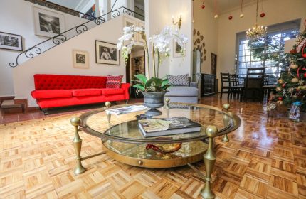 Casa Comtesse's gay-friendly hotel interior. A luxurious living room with a red sofa, glass table, and staircase. Upscale travel for gay men.