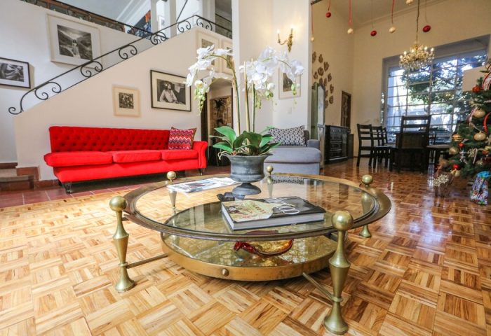 Casa Comtesse's gay-friendly hotel interior. A luxurious living room with a red sofa, glass table, and staircase. Upscale travel for gay men.