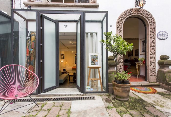 Casa Comtesse, a gay-friendly hotel. Exterior view with an open glass doorway, stone archway, and pink chair. Boutique hotel travel advice.