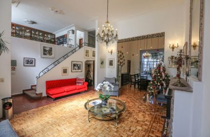 Casa Comtesse's interior, a gay-friendly hotel. Living room with red sofa, staircase, chandelier, Christmas tree, and parquet floor. Elegant design.