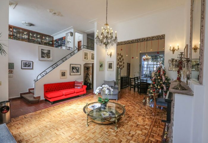 Casa Comtesse's interior, a gay-friendly hotel. Living room with red sofa, staircase, chandelier, Christmas tree, and parquet floor. Elegant design.