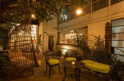 Casa Comtesse gay-friendly hotel patio at night. Wicker swing chair, iron table and chairs with cushions, and garden. Gay travel advice.