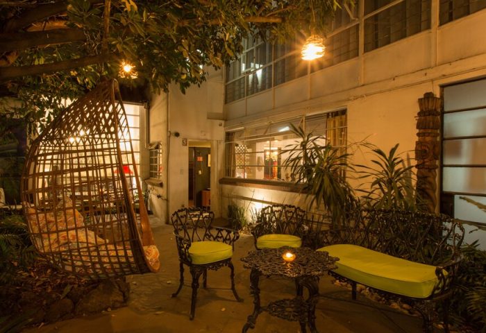 Casa Comtesse gay-friendly hotel patio at night. Wicker swing chair, iron table and chairs with cushions, and garden. Gay travel advice.