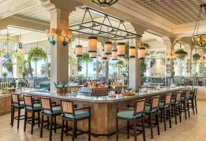 Casa Del Mar gay-friendly hotel bar. A bar with stools, hanging lights, and liquor bottles. Ocean view in background. Gay travel.