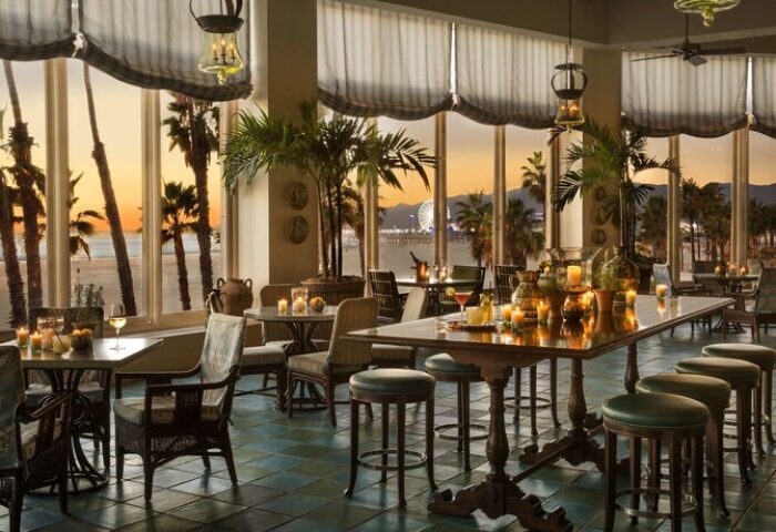 Casa Del Mar gay-friendly hotel interior. Ocean view dining room with palm trees, beach, pier, and sunset. Upscale travel for gay men.