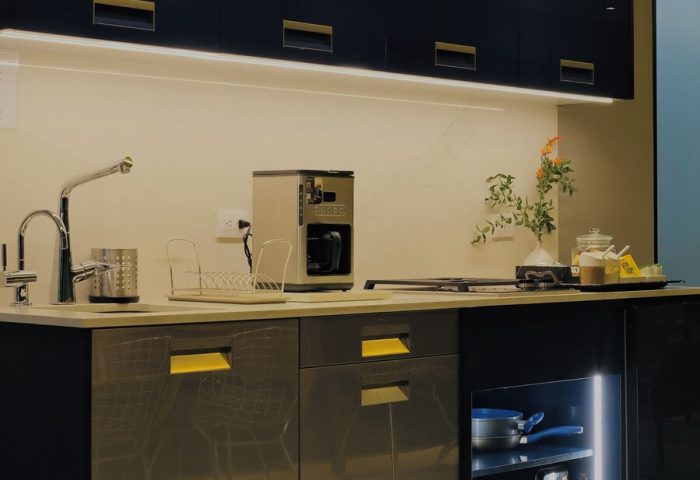 Casa Mannach gay-friendly hotel kitchen. Modern design with dark cabinets, gold accents, and under-cabinet lighting. Coffee maker, sink, and storage.