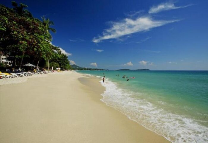 Beach view at Centara Grand Beach Resort Samui, a gay-friendly hotel. White sand, clear turquoise water, and blue sky. Perfect for gay travel.