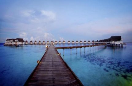 Centara Grand Island Resort & Spa, Maldives. A gay-friendly hotel with overwater bungalows connected by a long wooden pier. Blue water.