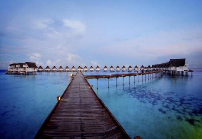 Centara Grand Island Resort & Spa, Maldives. A gay-friendly hotel with overwater bungalows connected by a long wooden pier. Blue water.