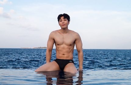 Gay-friendly Centara Grand Island Resort & Spa, Maldives. Fit Asian man in swimwear at the edge of an infinity pool overlooking the ocean.