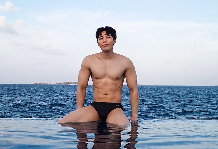 Gay-friendly Centara Grand Island Resort & Spa, Maldives. Fit Asian man in swimwear at the edge of an infinity pool overlooking the ocean.