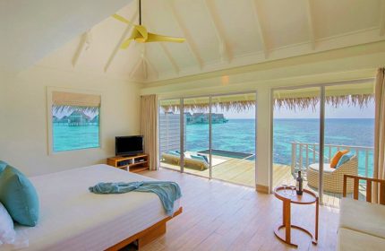 Centara Grand Island Resort & Spa Maldives room. Ocean view from gay-friendly hotel. Bedroom with a deck, pool, and lounge chair.