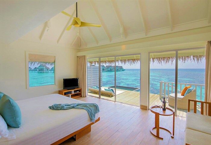 Centara Grand Island Resort & Spa Maldives room. Ocean view from gay-friendly hotel. Bedroom with a deck, pool, and lounge chair.