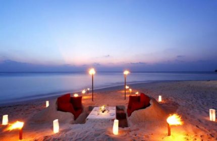 Romantic beach dinner at Centara Ras Fushi Resort & Spa, Maldives. Gay-friendly hotel with ocean view, torches, and red seating. Perfect for gay travel.