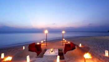 Romantic beach dinner at Centara Ras Fushi Resort & Spa, Maldives. Gay-friendly hotel with ocean view, torches, and red seating. Perfect for gay travel.