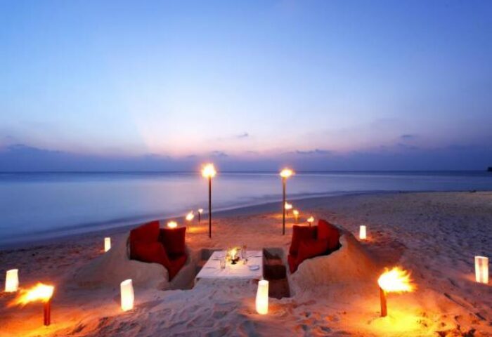 Romantic beach dinner at Centara Ras Fushi Resort & Spa, Maldives. Gay-friendly hotel with ocean view, torches, and red seating. Perfect for gay travel.