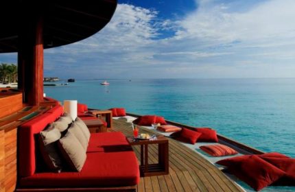 Centara Ras Fushi Resort & Spa Maldives gay-friendly hotel. Ocean view from a deck with red couches and pillows, perfect for relaxing.