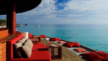 Centara Ras Fushi Resort & Spa Maldives gay-friendly hotel. Ocean view from a deck with red couches and pillows, perfect for relaxing.