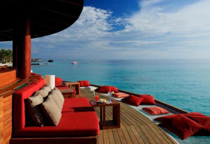 Centara Ras Fushi Resort & Spa Maldives gay-friendly hotel. Ocean view from a deck with red couches and pillows, perfect for relaxing.