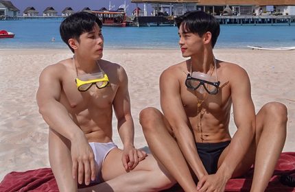 Gay couple at Centara Ras Fushi Resort & Spa Maldives. Men on beach with goggles, swimsuits, and villas in background. Gay-friendly hotel.