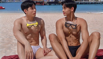 Gay couple at Centara Ras Fushi Resort & Spa Maldives. Men on beach with goggles, swimsuits, and villas in background. Gay-friendly hotel.