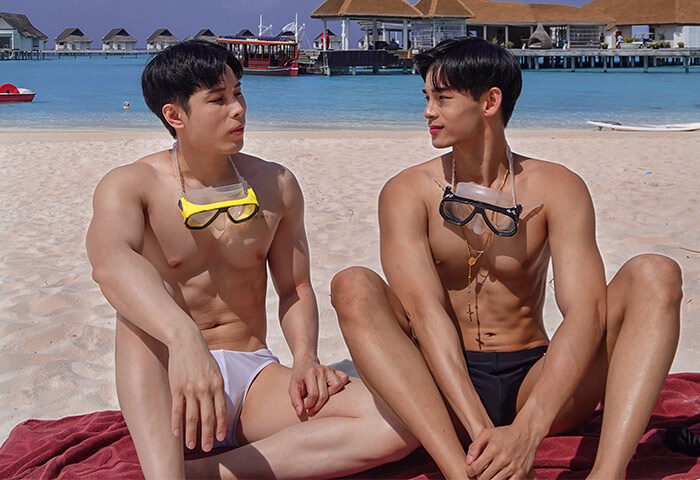 Gay couple at Centara Ras Fushi Resort & Spa Maldives. Men on beach with goggles, swimsuits, and villas in background. Gay-friendly hotel.