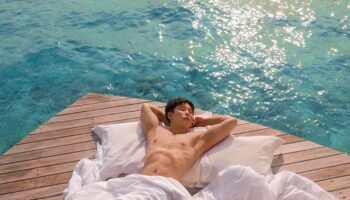 Gay-friendly Centara Ras Fushi Resort & Spa Maldives: Man relaxing on a deck over turquoise water. Ideal gay travel destination.