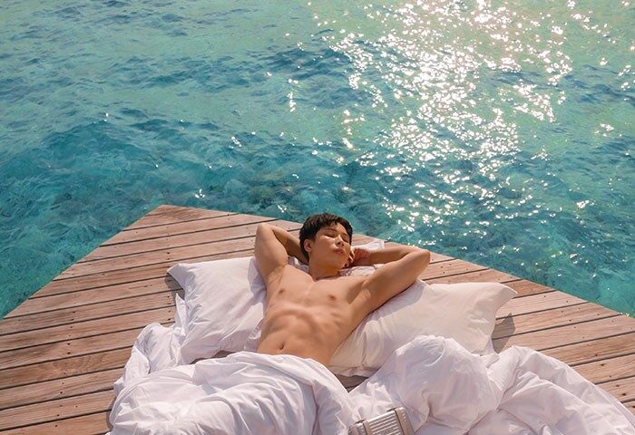 Gay-friendly Centara Ras Fushi Resort & Spa Maldives: Man relaxing on a deck over turquoise water. Ideal gay travel destination.