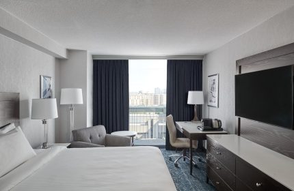 Chelsea Hotel Toronto guest room. Gay-friendly hotel featuring a bed, desk, TV, and balcony with city view. Modern decor.