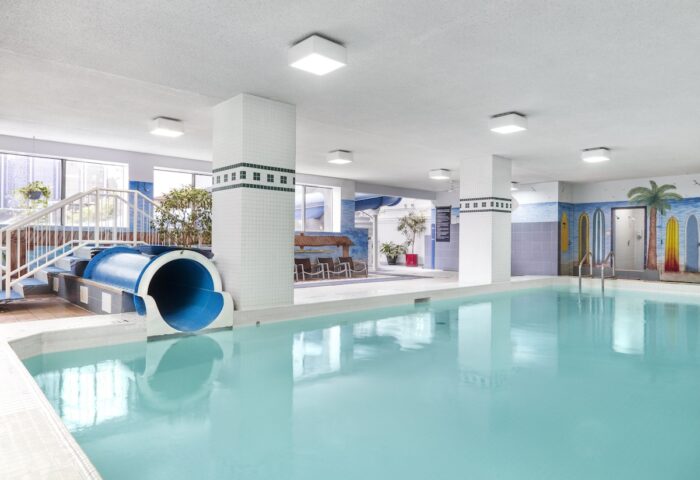 Indoor pool with slide at Chelsea Hotel Toronto, a gay-friendly hotel. Palm tree mural and surfboards decorate the wall.