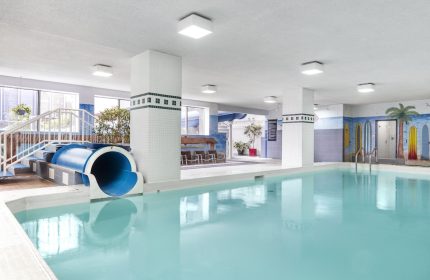 Indoor pool with slide at Chelsea Hotel Toronto, a gay-friendly hotel. Palm tree mural and surfboards decorate the wall.