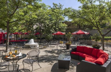 Chelsea Hotel Toronto's gay-friendly outdoor patio. Tables, chairs, red umbrellas, and a fountain create a relaxing space. Perfect for gay travelers.