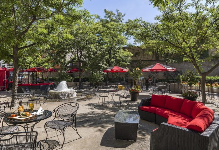 Chelsea Hotel Toronto's gay-friendly outdoor patio. Tables, chairs, red umbrellas, and a fountain create a relaxing space. Perfect for gay travelers.