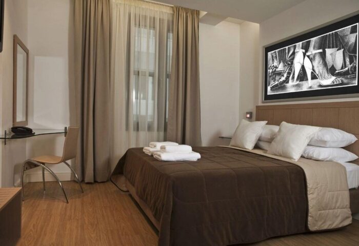 Gay-friendly Chic Hotel room with brown bedding, white pillows, and a suggestive art piece above the bed. Modern design, inviting space.