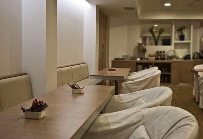 Chic Hotel dining area. Gay-friendly hotel with modern design. Tables with condiments, cushioned seating, and covered chairs. Breakfast buffet in background.