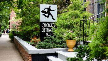 Chicago Getaway Hostel sign. Gay-friendly hotel with a man running with a suitcase logo. Lush greenery surrounds the entrance.