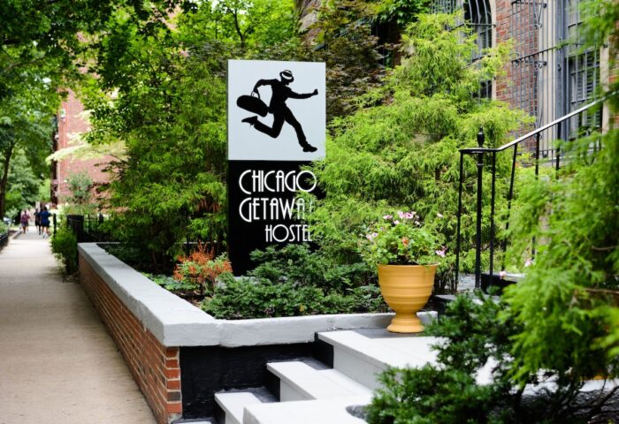 Chicago Getaway Hostel sign. Gay-friendly hotel with a man running with a suitcase logo. Lush greenery surrounds the entrance.