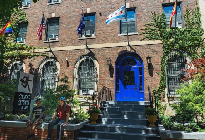 Chicago Getaway Hostel's exterior. Gay-friendly hotel with flags, including a rainbow flag. Two men are sitting outside the hostel.