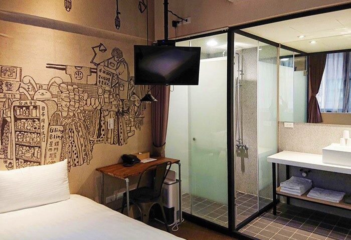 Cho Hotel room featuring a bed, desk, TV, and enclosed shower. The wall has a unique mural. Gay-friendly hotel for gay men travelers.