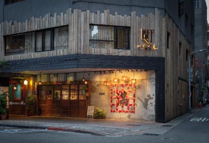 Exterior of Cho Hotel, a gay-friendly hotel. The building has a unique wooden facade and warm lighting, creating an inviting atmosphere.
