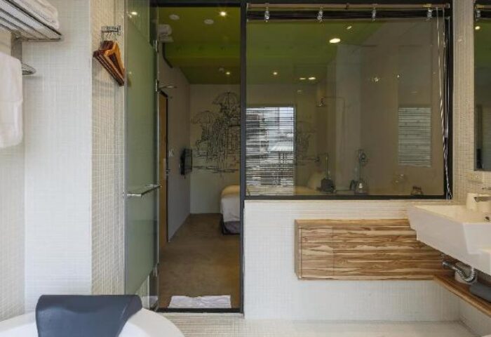 Cho Hotel bathroom interior. Modern design with glass partition, white tiles, and wooden accents. Gay-friendly hotel room detail.