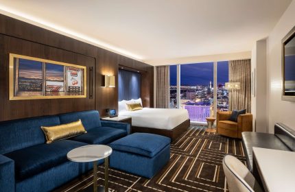 Circa Resort and Casino adults-only suite. Gay-friendly hotel room with Vegas skyline view, blue sofa, and slot machine artwork.