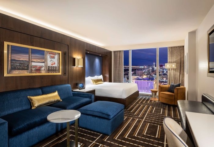 Circa Resort and Casino adults-only suite. Gay-friendly hotel room with Vegas skyline view, blue sofa, and slot machine artwork.