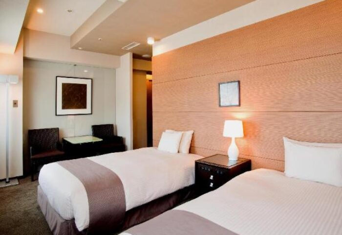 Citadines Central Shinjuku Tokyo: Twin beds in a gay-friendly hotel room. Features bedside table, lamp, seating area, and modern decor.
